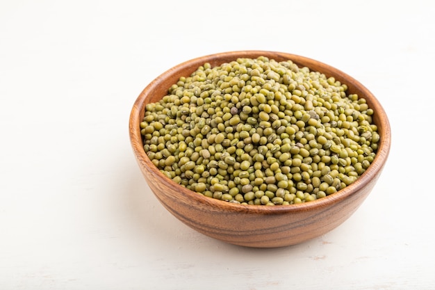 Photo wooden bowl with raw green mung bean on a white wooden background. side view.