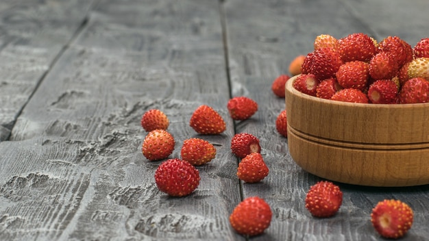 A wooden bowl with ripe wild strawberries on a wooden table. Fresh crop.