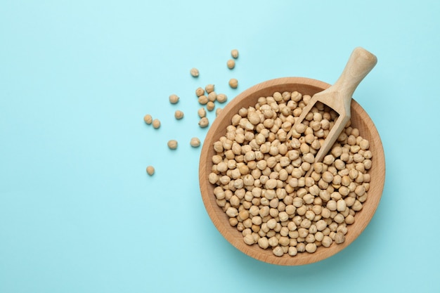 Wooden bowl with scoop and chickpea on blue background