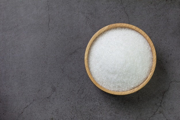 Wooden bowl with sugar on black concrete