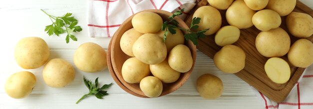 Wooden bowl with young potato on white wooden table