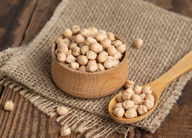 Wooden bowl and wooden spoon full of chickpeas on a wooden\
background