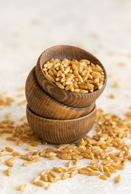 Wooden bowls of raw dry rye grain on white table close up