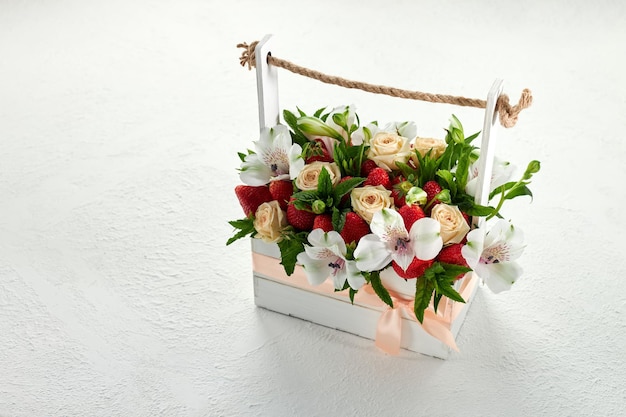 写真 熟したイチゴと白い背景の上の美しい白とピンクの花でいっぱいの木箱