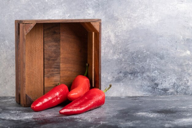 Wooden box of fresh red chili peppers on marble.