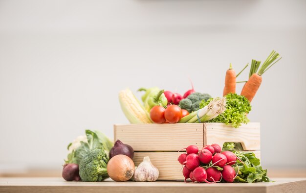 Wooden box full of fresh healthy vegetables. Broccoli carrot radish onion garlic corn on wooden kitchen table.