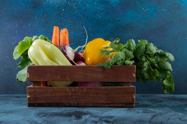 Wooden box of healthy fresh vegetables on blue wall.