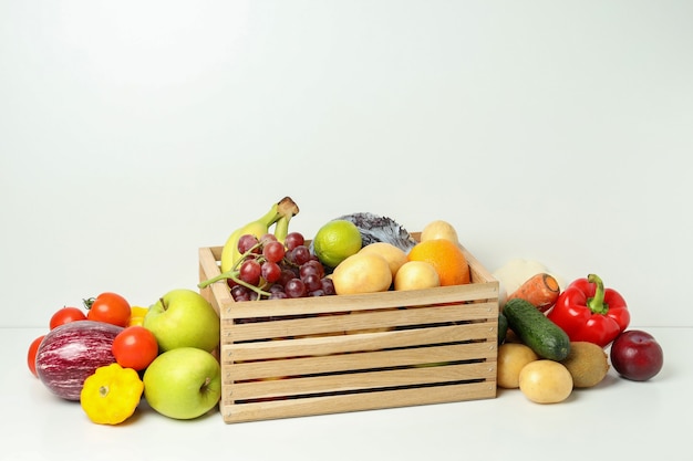 Wooden box with different vegetables and fruits on white table