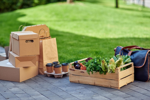 Wooden box with fresh grocery four paper coffee cups various\
packages and boxes with food