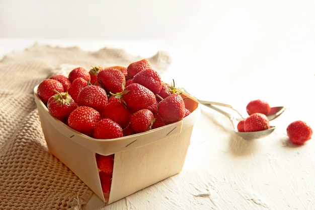 Wooden box with fresh strawberries on white background with linen napkin