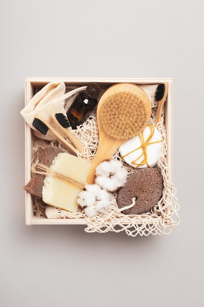 Wooden box with reusable cosmetic accessories on a gray background. Organic soap, brushes, pumice stone, bottle, cotton pads. Top view