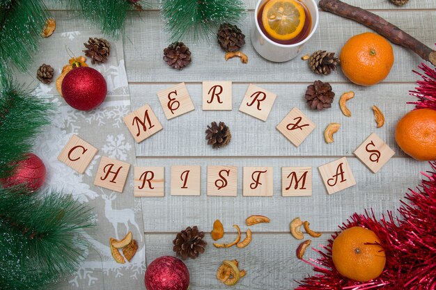 Wooden boxes with the inscription merry christmas, pine\
branches, christmas toys, tangerines, tea with lemon, christmas\
mood, top view, wooden background