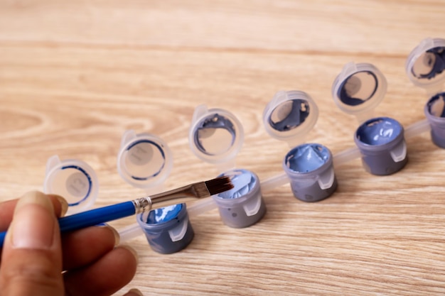 写真 wooden brush held by hand near electric blue paint bottles