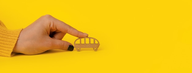 Wooden bus in hand over yellow background, transportation concept, panoramic mock-up