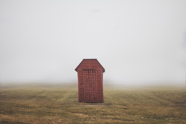 Photo wooden cabin on grassy filed against sky during foggy weather