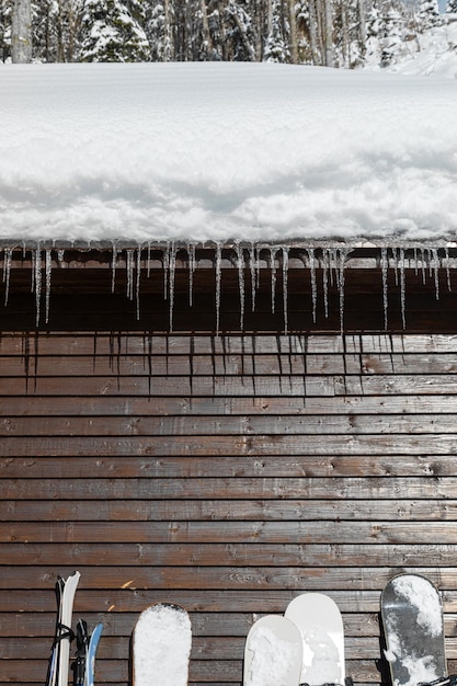 Wooden cabin with snowy roof and icicles and ski equipment leaning against the wall