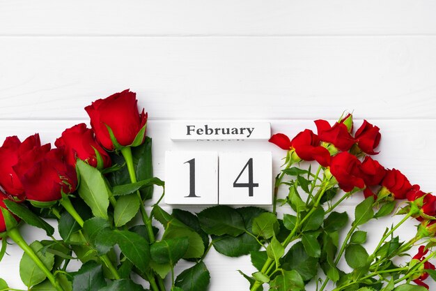 Wooden calendar 14th February and roses on white background flat lay