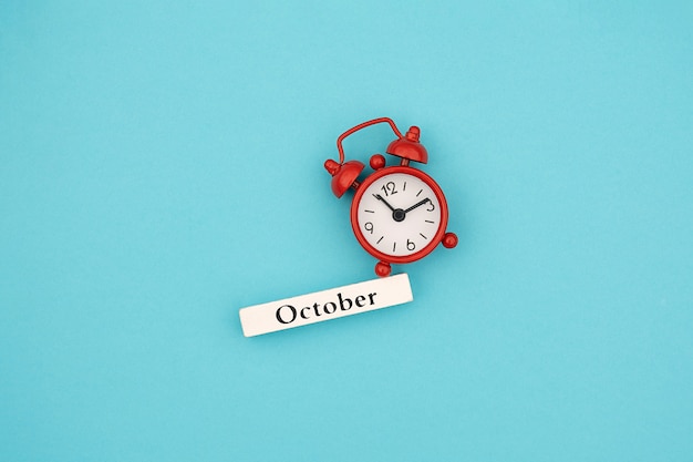 Wooden calendar autumn month October and red alarm clock on blue