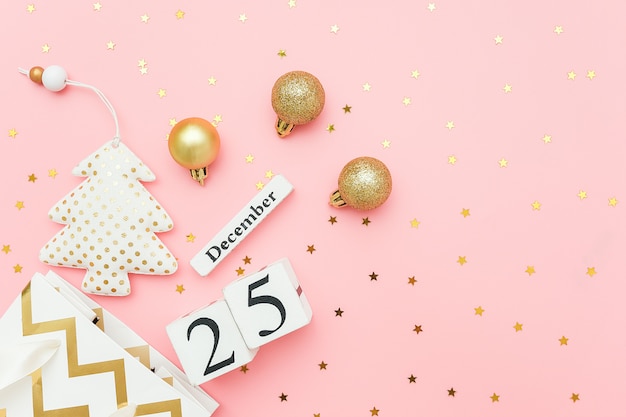 Деревянный календарь 25 декабря, текстильная елка, золотые безделушки, звезды конфетти на розовом. Счастливого Рождества концепции.