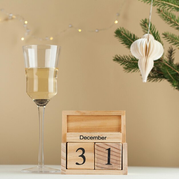 Wooden calendar december  new year background a glass of wine a tree branch a garland copy space min...