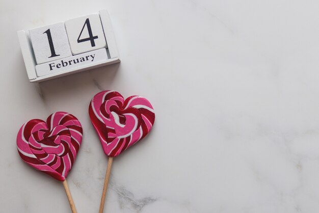 Wooden calendar February and heart shaped candies on marble