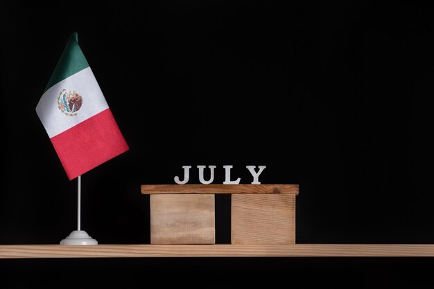 Wooden calendar of july with mexico flag on black background.