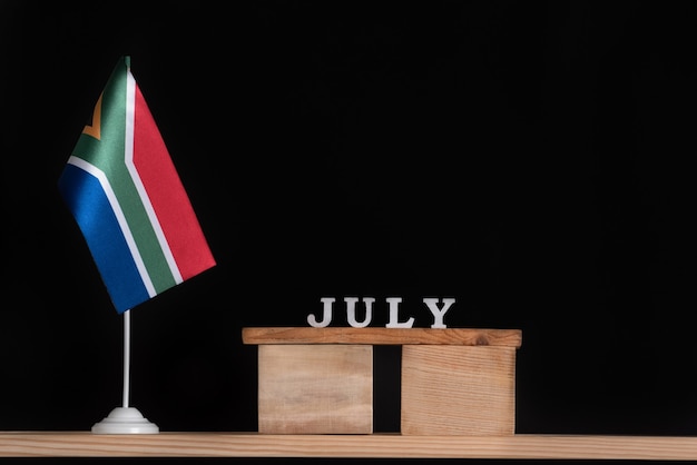 Wooden calendar of July with RSA flag on black background. Dates of South Africa in July .