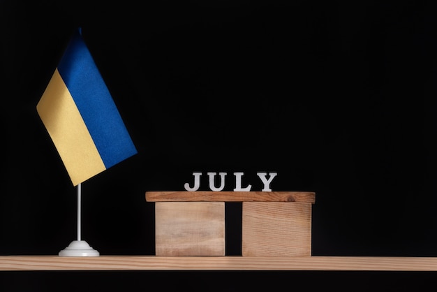 Wooden calendar of July with Ukrainian flag on black background. Dates in Ukraine in July.