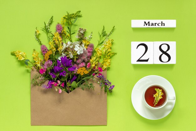 Wooden calendar March 28 Cup of tea, kraft envelope with multi colored flowers on green 