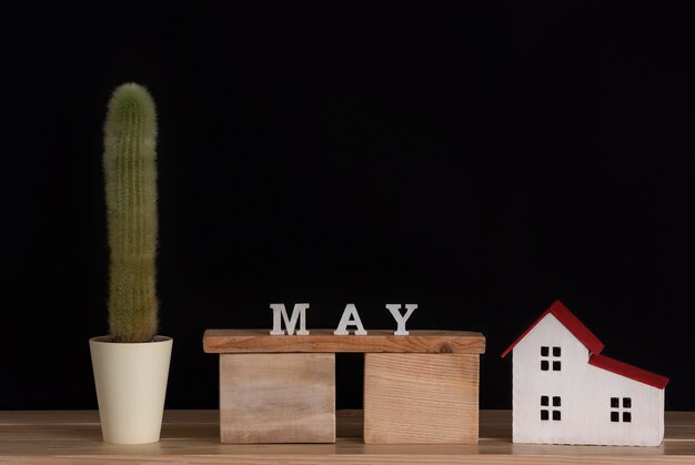 Wooden calendar of May, cactus and house model on black background. Copy space.