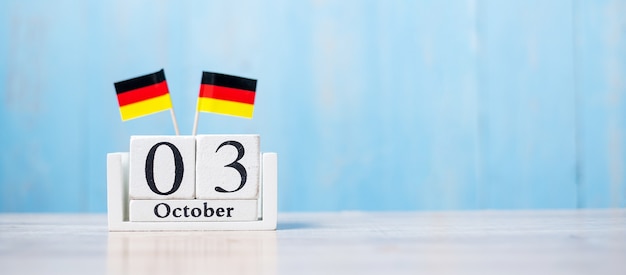 Wooden calendar of October 3rd with miniature Germany flags.