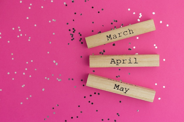 Wooden calendar spring months March, April, May. Pink background with multicolored confetti. Flat lay style