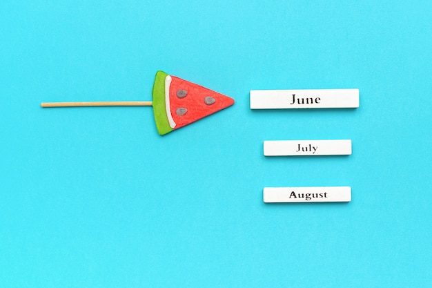 Photo wooden calendar summer months june, july, august and watermelon lollipop.