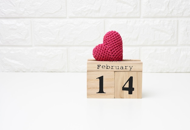 Wooden calendar with date February 14 and red knitted heart, white table