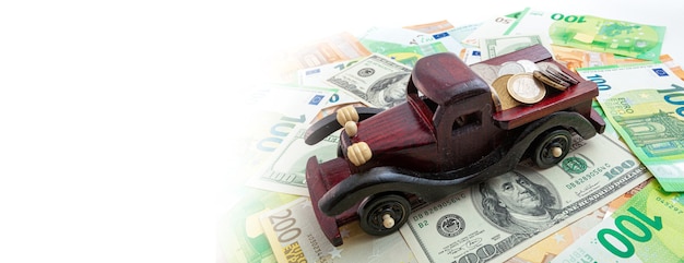 Wooden car with coins on euro and dollars texture background panorama