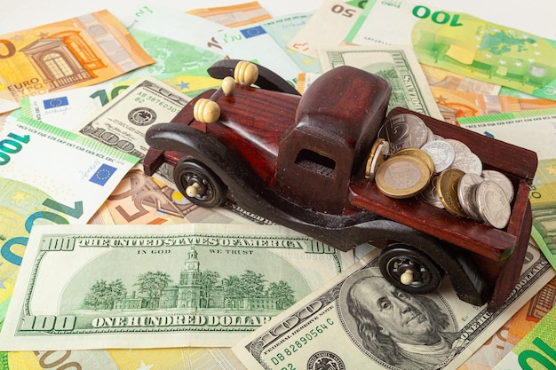 Wooden car with coins on euro and dollars texture background