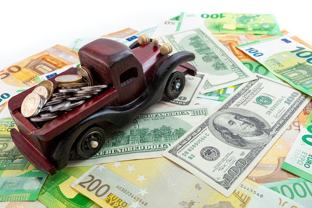 Wooden car with coins on euro and dollars texture background