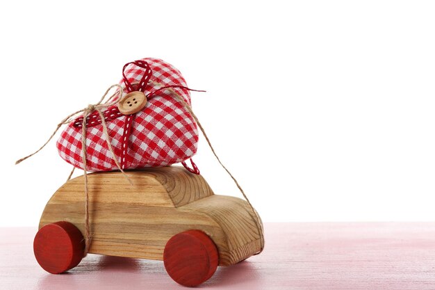 Wooden car with a red fabric heart tied to it on pink wooden table