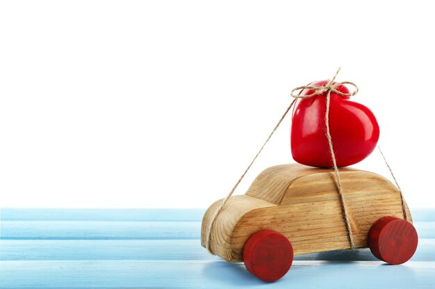 Wooden car with a red heart tied to it on a blue wooden table over white background