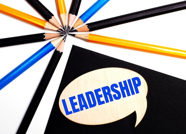 Wooden card with the text LEADERSHIP on a black background near multicolored pencils