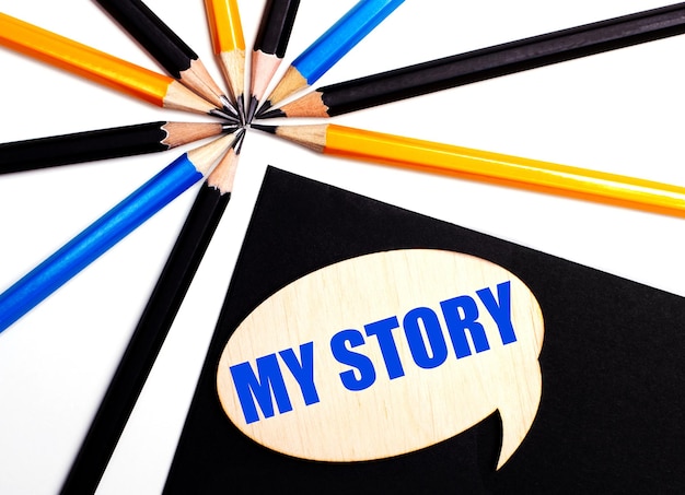 色とりどりの鉛筆の近くの黒の背景に「MY STORY」というテキストが記載された木製のカード