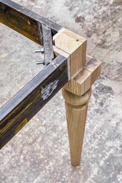 Wooden carved leg of solid oak with metal frame during manufacturing process of dining table