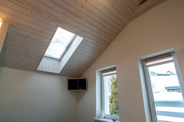 Wooden ceiling in a contemporary mansard room with attic window of decorative planks surface.