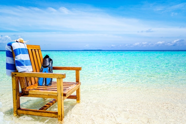 A wooden chair standing in the Indian Ocean with a towel shell and flippers