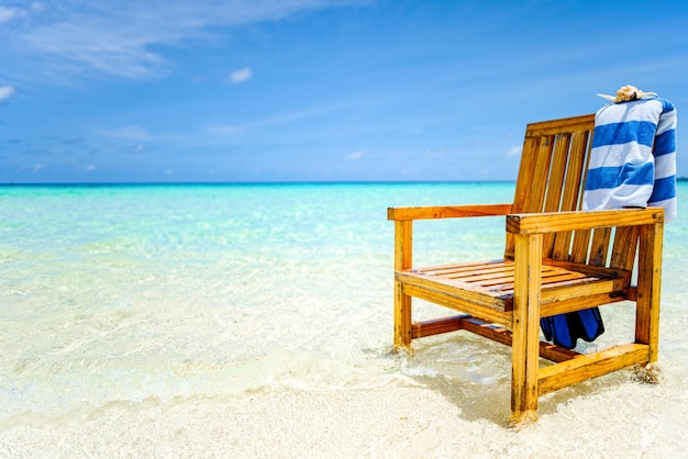 A wooden chair standing in the Indian Ocean with a towel shell and flippers