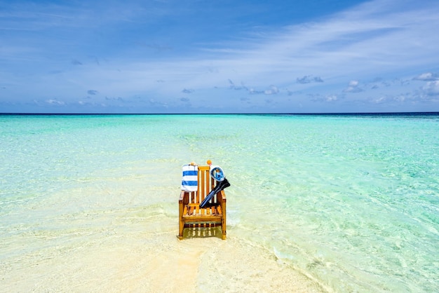 A wooden chair standing in the Indian Ocean with a towel shell and flippers