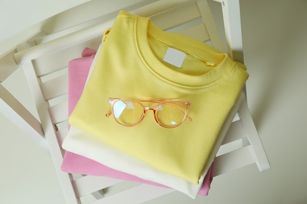 Wooden chair with yellow, pink and white sweatshirts and glasses