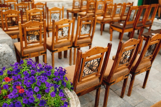 Wooden chairs with patterns on the backs stand in rows on paving stones