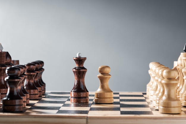 Деревянные шахматные фигуры на шахматной доске, противостояние белой пешки и черного ферзя, концепция планирования и принятия решений