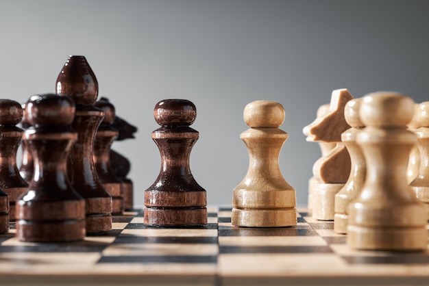 Wooden chess pieces on a chessboard, opposing pawns of different colors, the concept of strategy, planning and decision-making